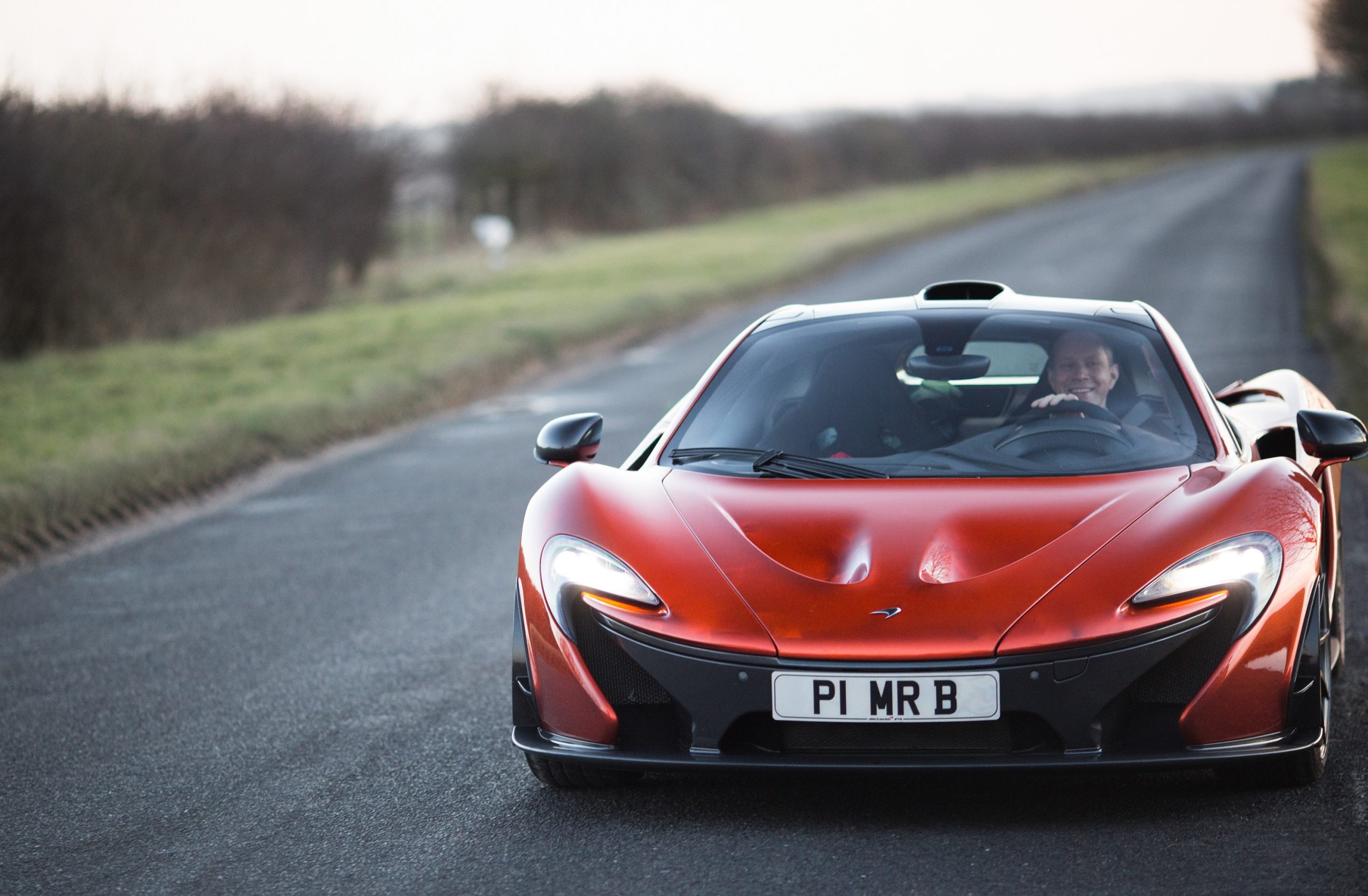 An orange McLaren P1 supercar shot from the front on a rainy day