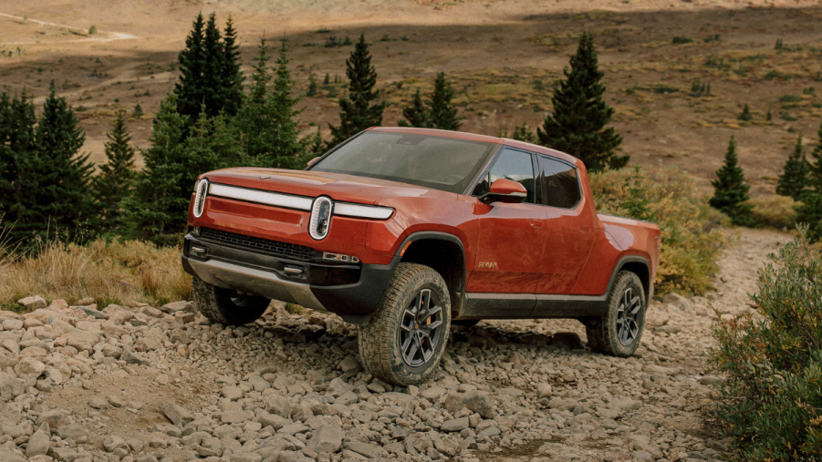 Orange 2022 Rivian R1T driving up a hill, highlighting reasons to buy an EV in 2022