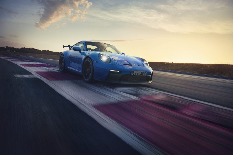 A 3/4 front view of a blue 2022 Porsche 911 GT3 cornering on a race track with a sunset in the background.