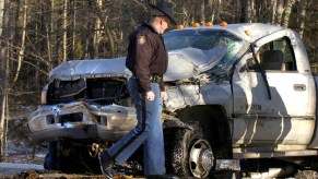 Police officer looking at the caved-in grille of a smashed Ram truck.