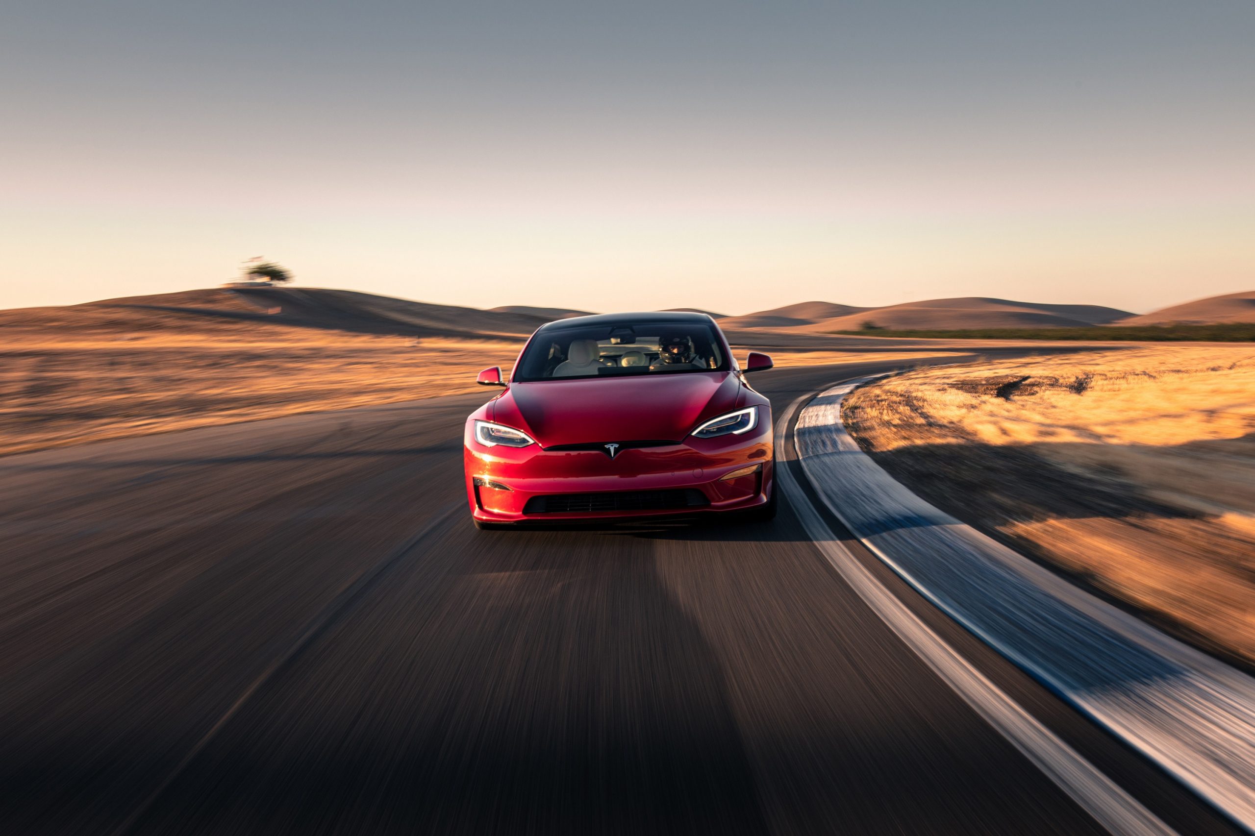 A Tesla Model S Plaid electric car shot from the front on a race track at sunset