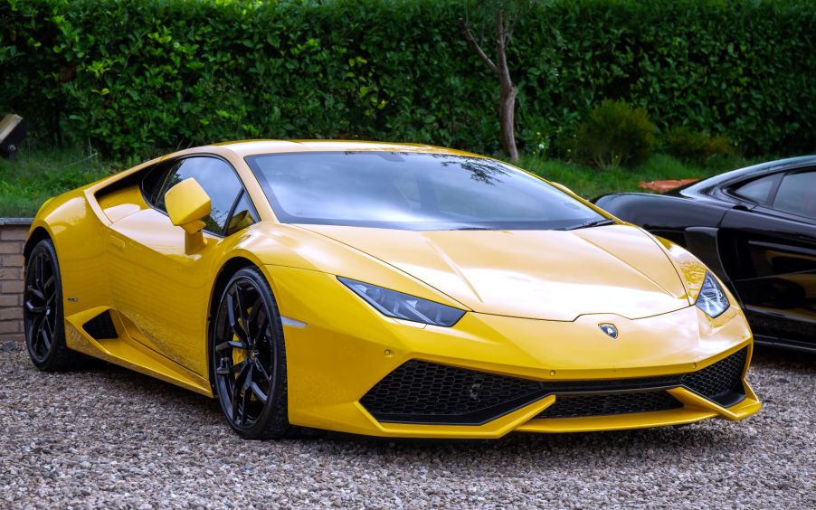 A yellow Lamborghini Huracan sitting on gravel in front of a wooded area.