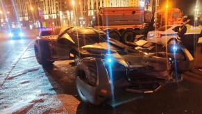 A batmobile replica surrounded by cops on the street in Russia, at night.