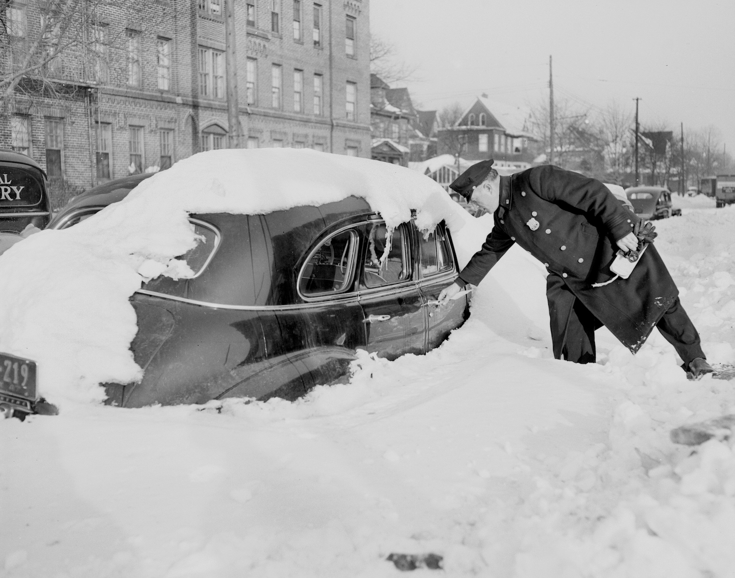 This is a police officer ticketing a snow-covered car for violating a winter parking ban on a city street.