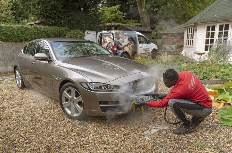 Man steam cleaning a luxury car on a home visiting valet service, England UK