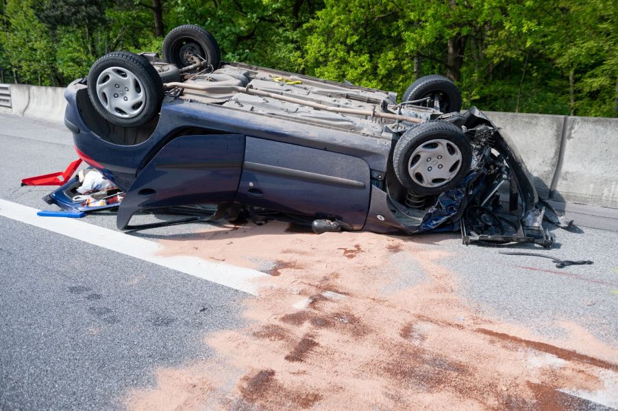 A rollover car accident on the side of the road with the car upside down.