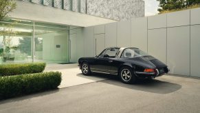 A rear 3/4 view of a black 1972 Porsche 911 S Targa by the Porsche Design building