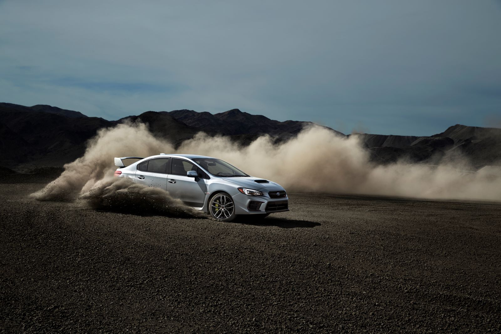 Silver 2020 Subaru WRX STI drifting around a tight corner, throwing up dust and dirt behind its rear wheels