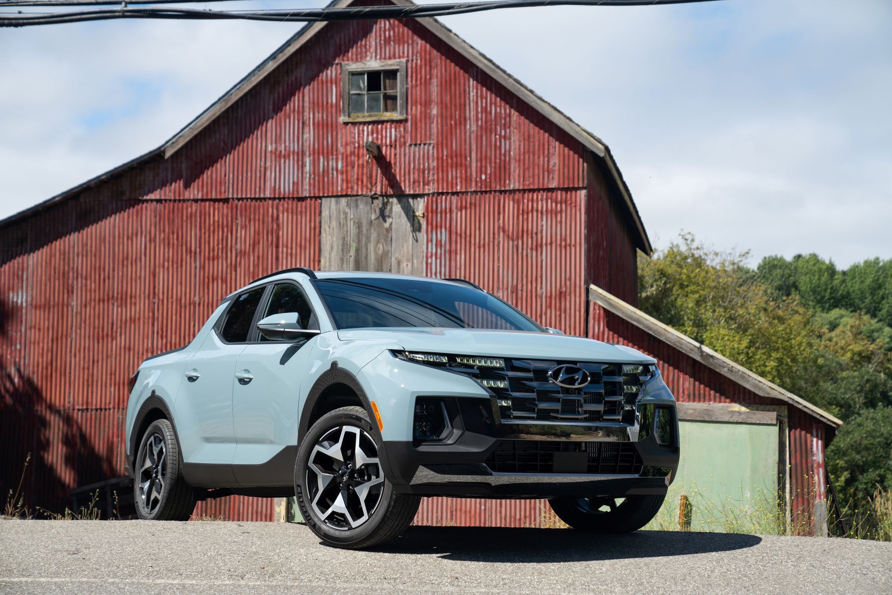 2022 Hyundai Santa Cruz compact pickup truck in light blue parked in front of a steel barn