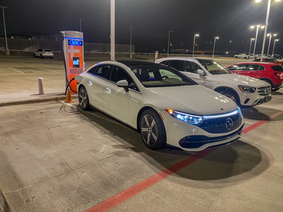 The front 3/4 view of a white 2022 Mercedes EQS 450+ charging in a Mercedes dealership lot