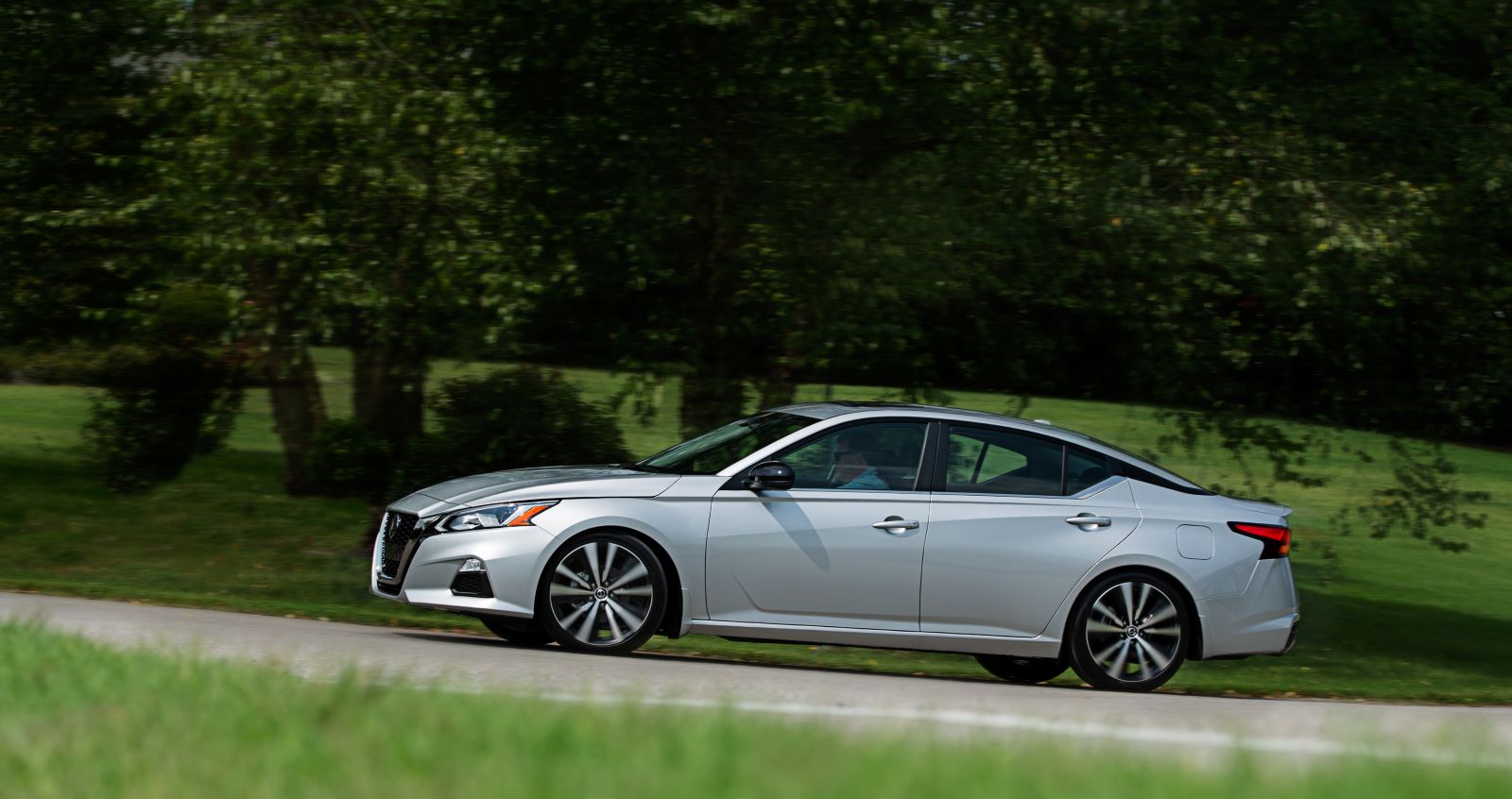 Side profile of a 2022 Nissan Altima all-wheel-drive sedan in silver, shown driving on a dirt road in the country