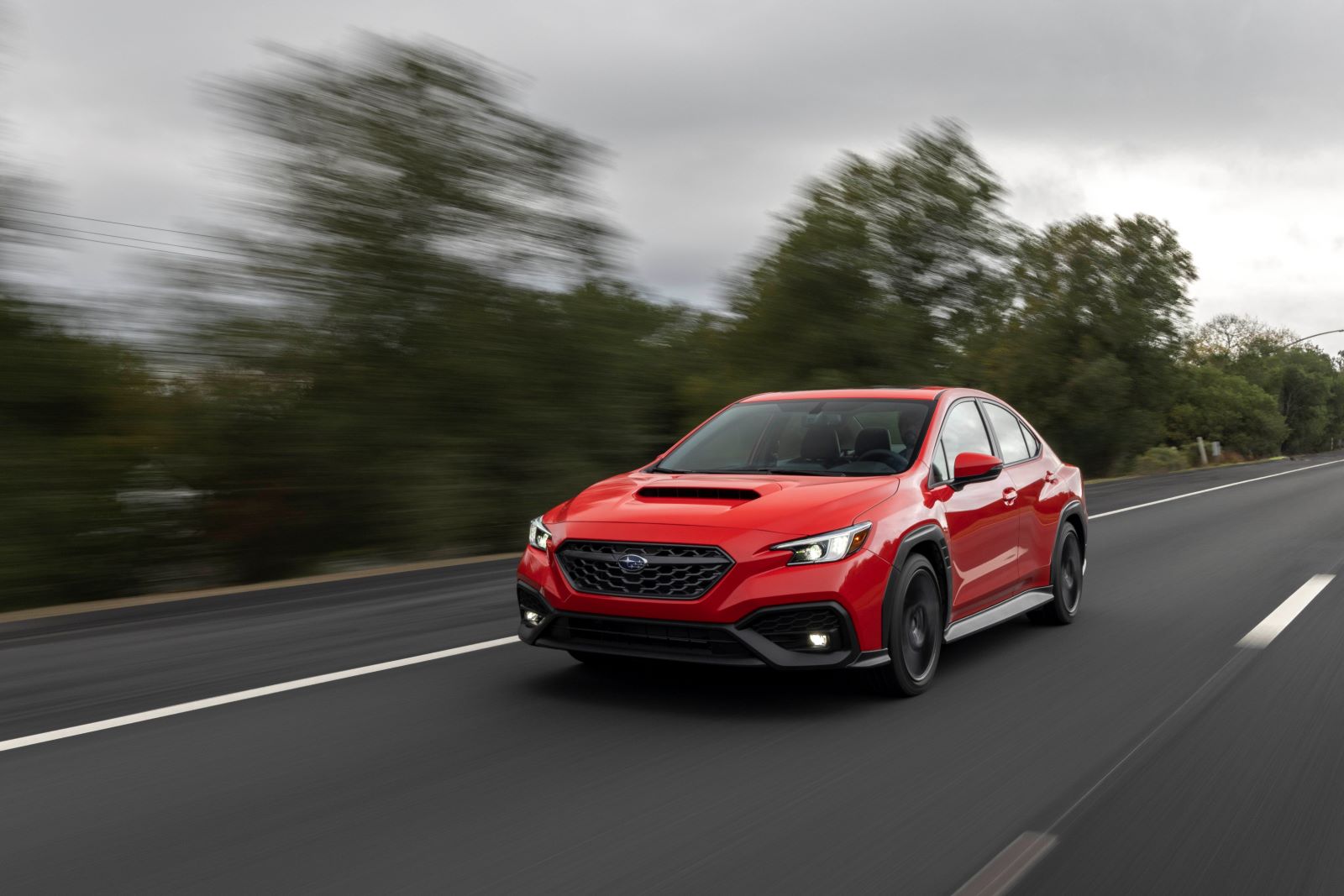 A red 2022 Subaru WRX speeds down a highway on a grey and overcast day