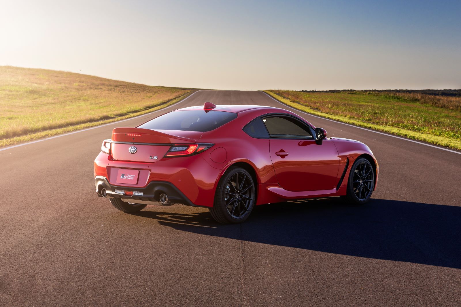 Red 2022 Toyota GR86 sports car parked on a long asphalt road. Picture taken from a rear angle