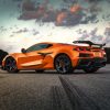 A 3/4 rear view of an orange 2023 Chevrolet Corvette Z06 parked on a road with trees in the background.