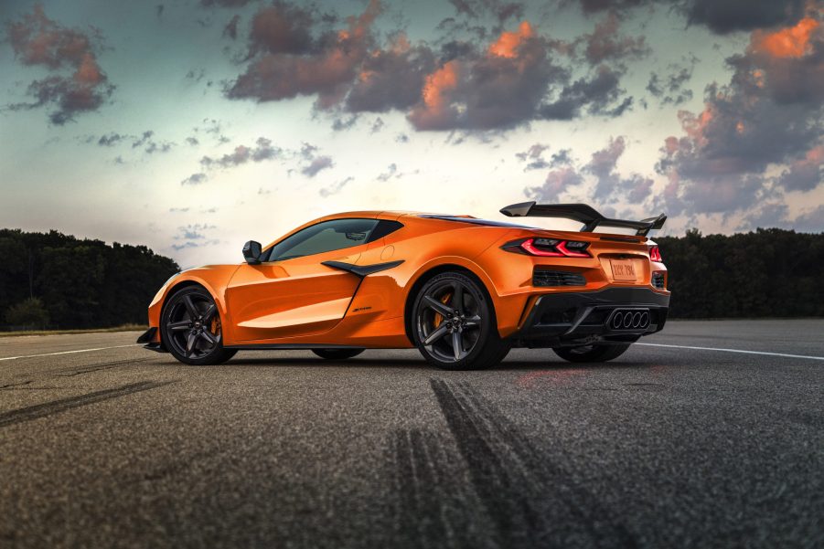 A 3/4 rear view of an orange 2023 Chevrolet Corvette Z06 parked on a road with trees in the background.