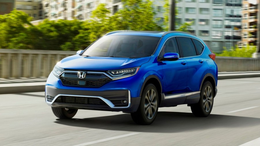 Aegean Blue Metallic 2022 Honda CR-V driving by a large building