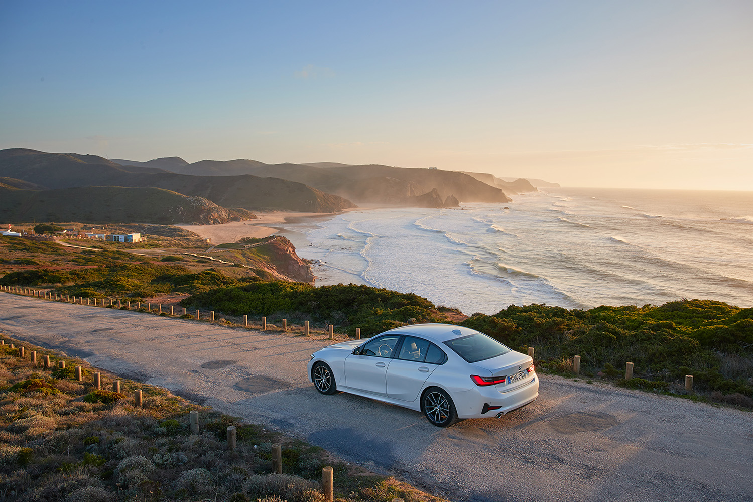 BMW 3 Series on beach coastal highway with sunset in the bakcground