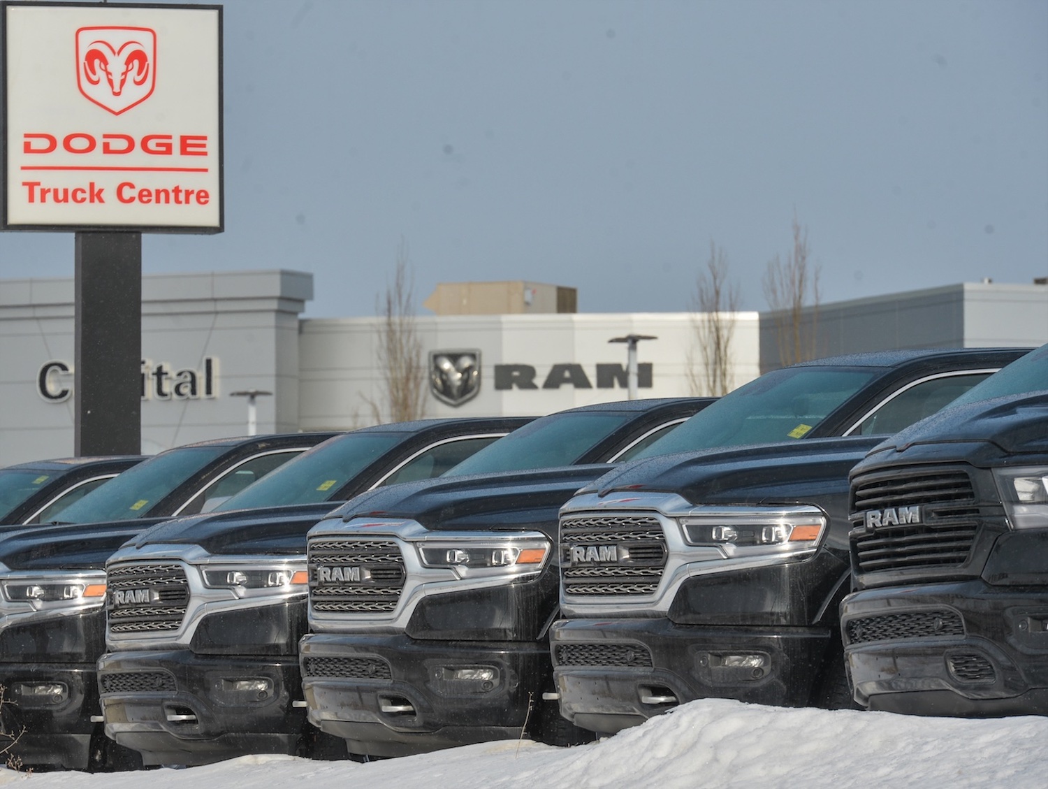 Row of fifth generation Ram trucks parked in front of an old "Dodge Truck Centre" sign at a dealership