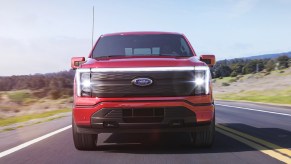 A red 2022 Ford F-150 Lightning is driving down the road.