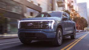 A blue 2022 Ford F-150 Lightning electric pickup truck is driving down the road.