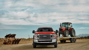 Red heavy-duty Ford truck towing a tractor on a trailer.