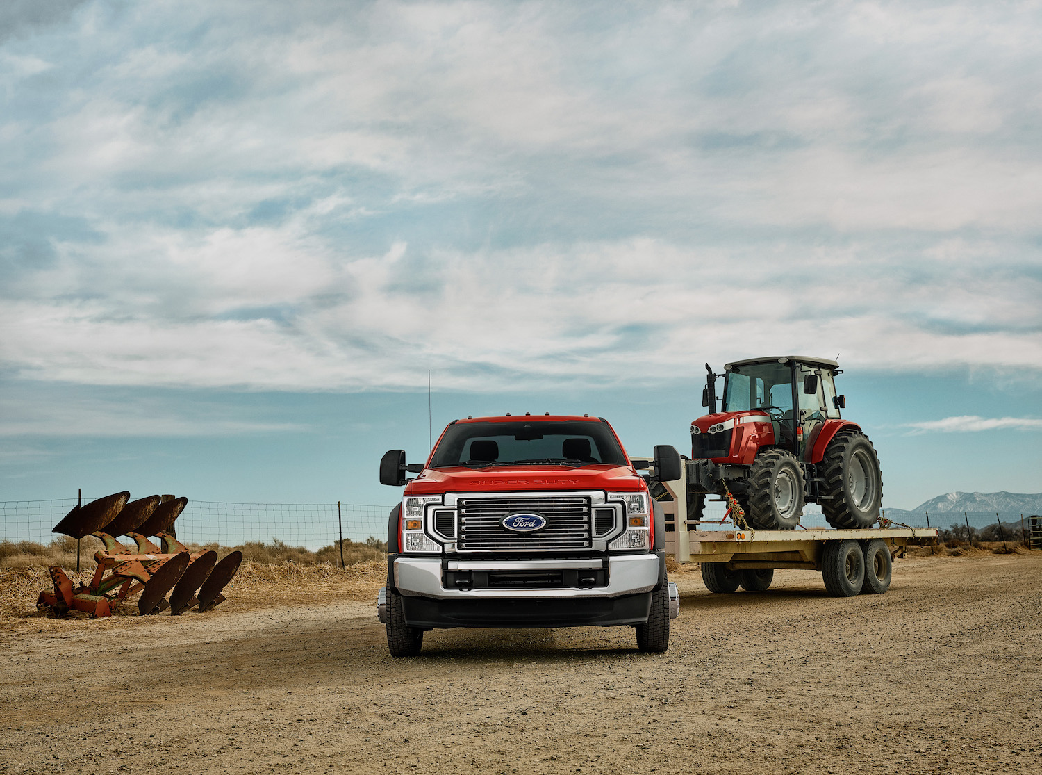 Red heavy-duty Ford truck towing a tractor on a trailer.