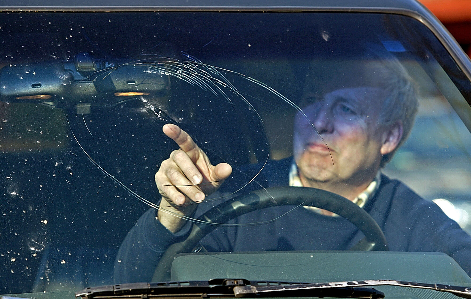 A man points out the crack in his car's windshield. Is it dangerous to drive this way?