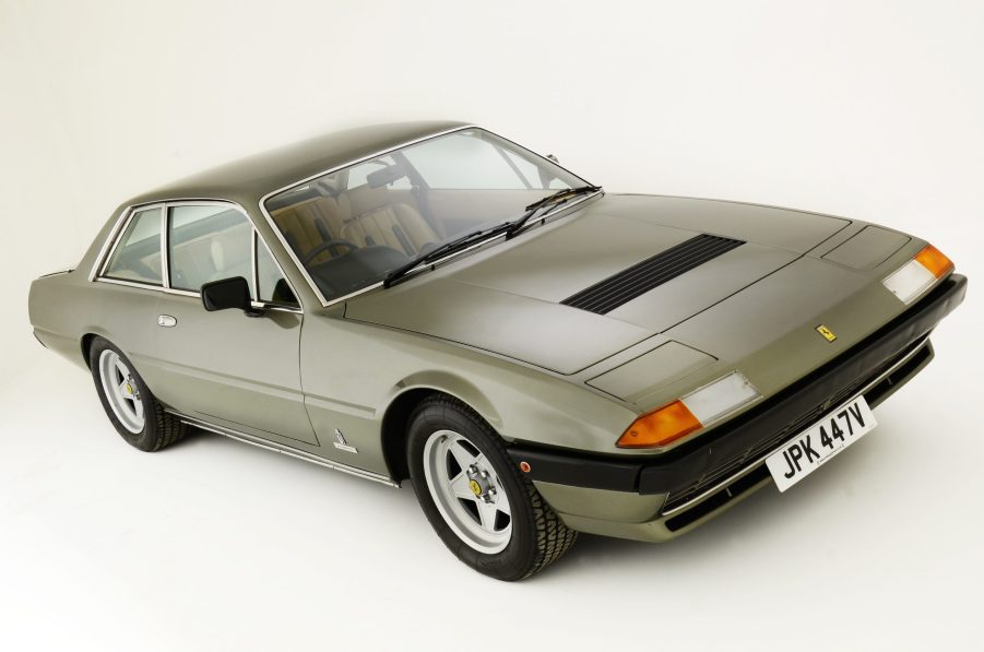 A 3/4 front and overhead view of a light brown 1980 Ferrari 400i with a white studio background