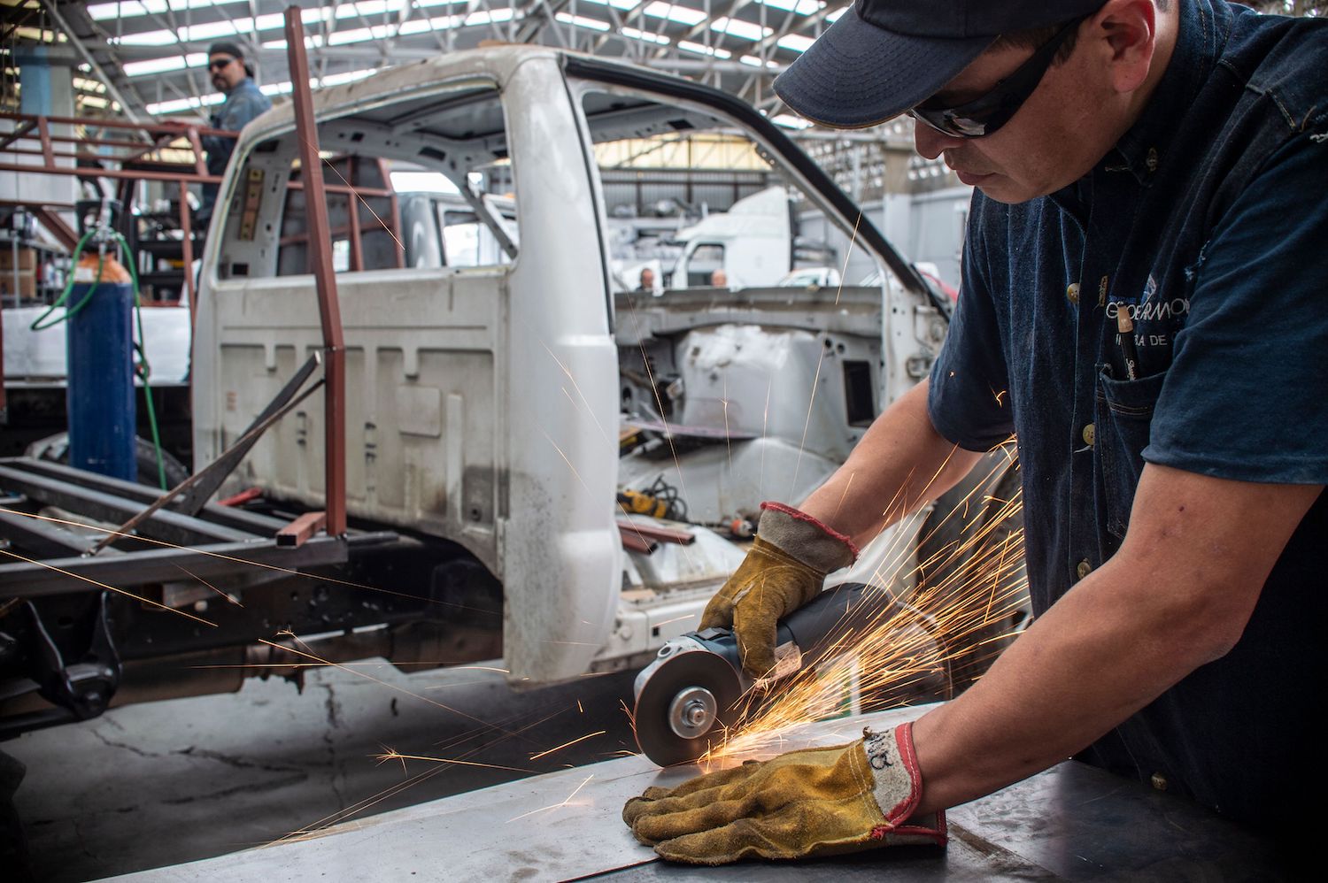 Mexican factory worker cuts a piece of metal while assembling a heavy-duty truck.