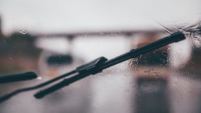 Wipers cleaning a wet windshield, a rainy road visible in the background.