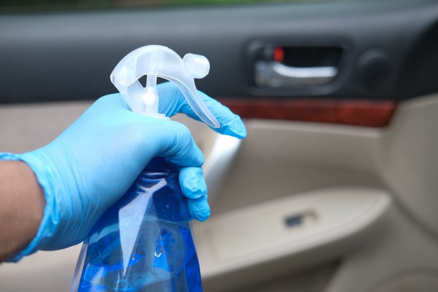 An automotive detailer's hand spraying a car interior with a cleaner.