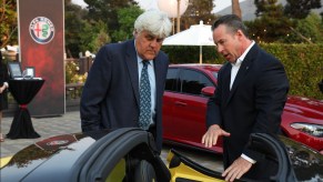 Jay Leno listening to the dealership pitch next to a yellow Alfa Romeo.