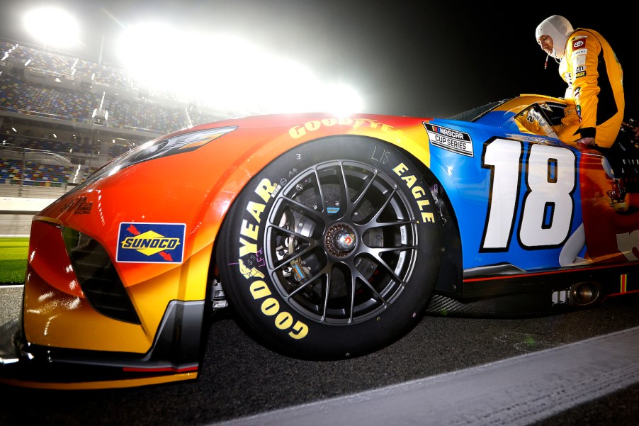 Closeup of a driver sliding into a NASCAR Next Gen car with the driver sliding into the cabin in the background.