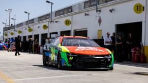 A NASCAR Next Gen race car parked in pit road, technicians standing in the background.