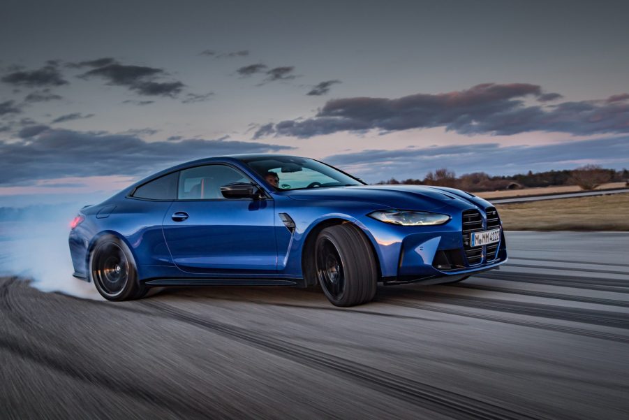 A blue BMW M4 Competition powersliding through a corner of a race track with smoke coming from the rear wheels.