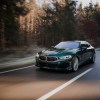 A 3/4 front view of a green Alpina B8 sedan driving on a tree-lined road.