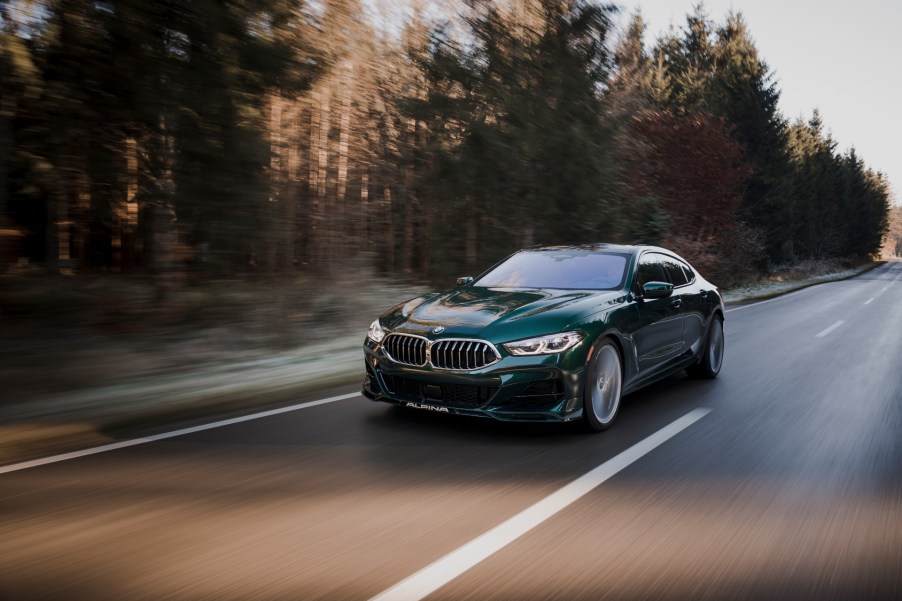 A 3/4 front view of a green Alpina B8 sedan driving on a tree-lined road.