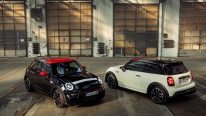 A view of a pair of MINI Pat Moss Edition Cooper JCW cars parked in a warehouse. A black car facing the camera and a white car facing away.