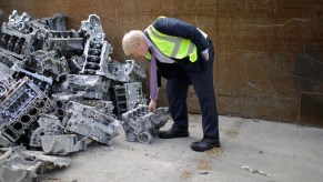 A man examines a V8 engine block in a pile of scrap.