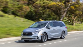 Silver 2022 Honda Odyssey, the U.S. News best minivan to buy for families in 2022, driving by a forest