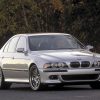 A silver E39 BMW M5 parked on a road next to a forest