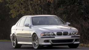 A silver E39 BMW M5 parked on a road next to a forest