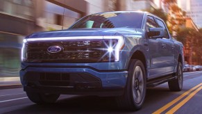 A blue 2022 Ford F-150 Lightning electric pickup truck is driving on the road.