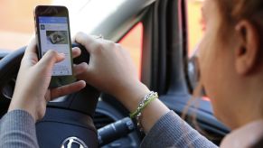 A woman texting and browing Twitter on her smartphone while driving a motor vehicle