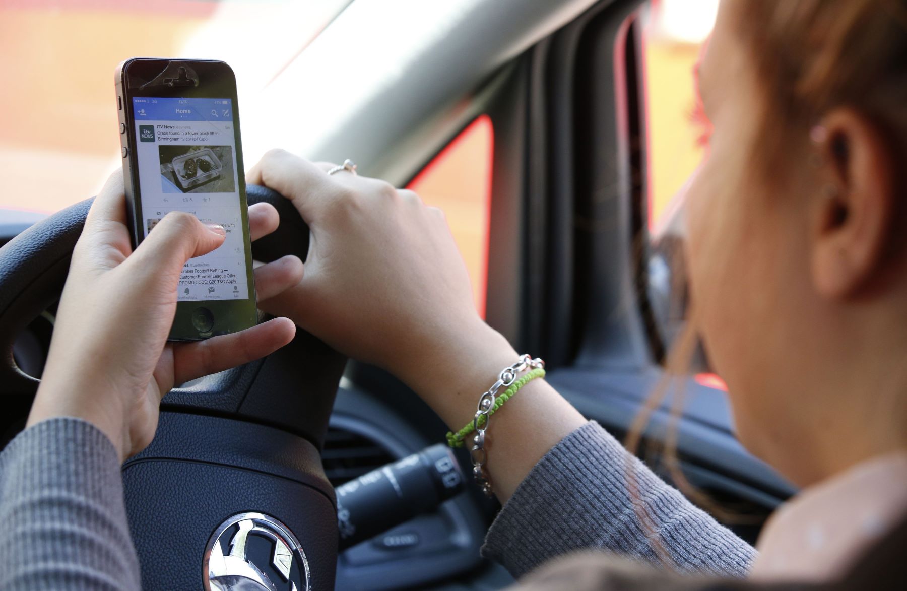 A woman texting and browing Twitter on her smartphone while driving a motor vehicle