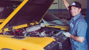 Smiling mechanic holding up the hood of a bright yellow Land Rover SUV.