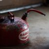 An old metal gas can, its paint peeling off, sitting on a stained concrete floor.