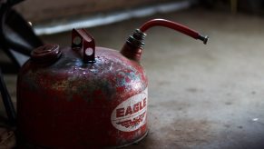 An old metal gas can, its paint peeling off, sitting on a stained concrete floor.