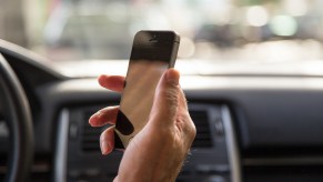 Man driving car and checking the smartphone in first person view.