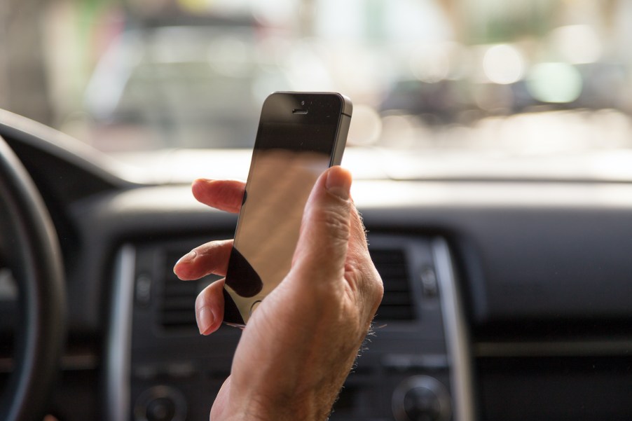 Man driving car and checking the smartphone in first person view.